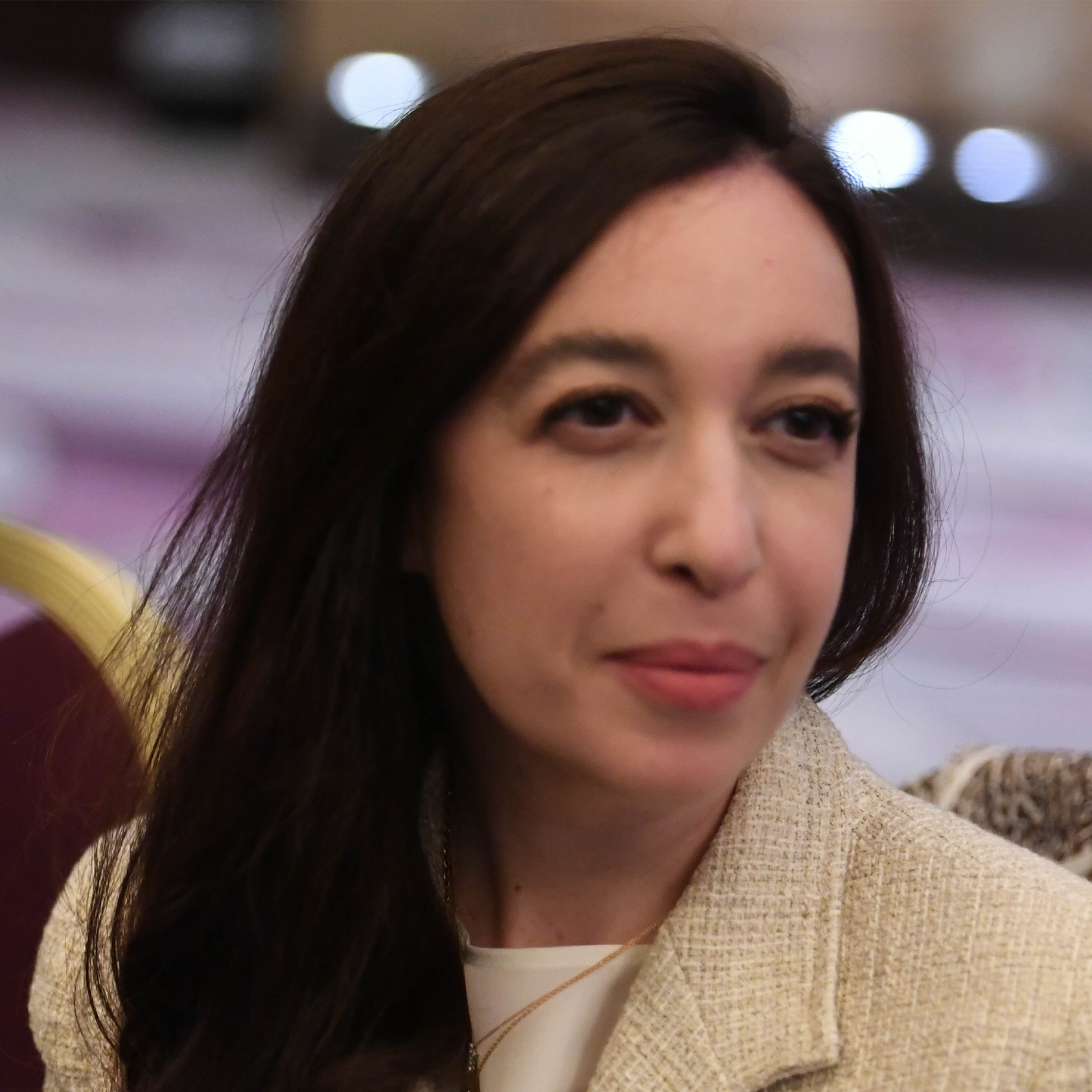 Lynn Zovighian with long dark hair, wearing a white top and beige blazer, looking slightly to her right.