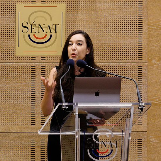 Lynn Zovighian speaking at a podium at the Palace of Luxembourg during a Yazidi Genocide conference.