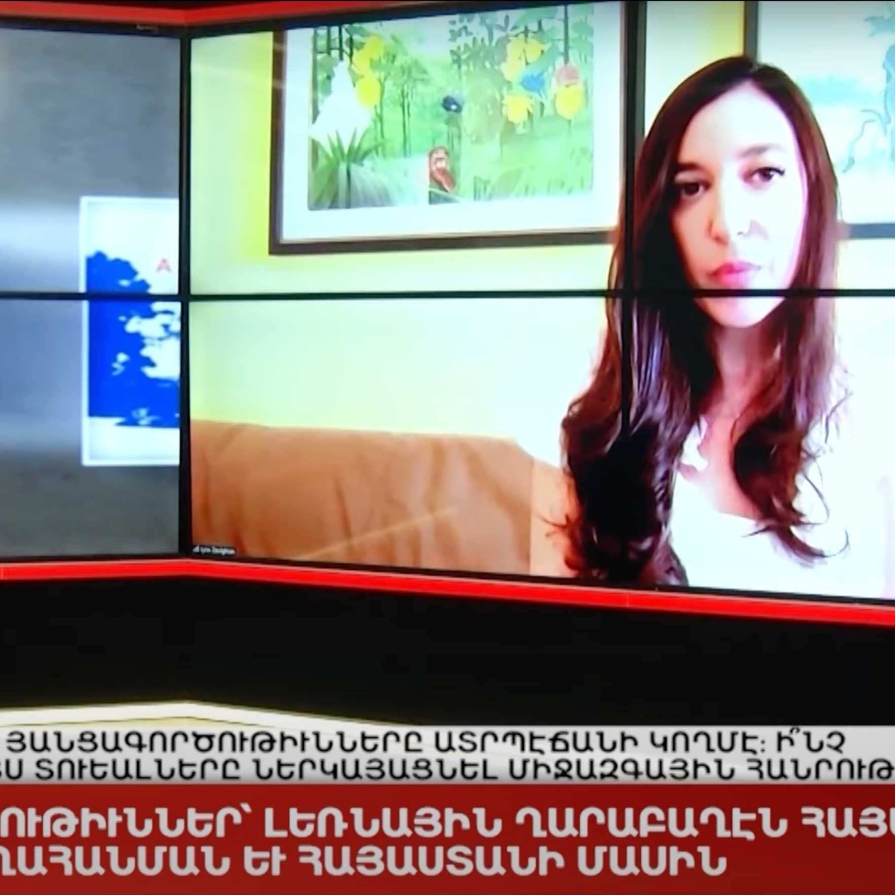 Lynn Zovighian in a video interview with Armenian Public TV visible on a screen, set in a studio with text in Armenian below.