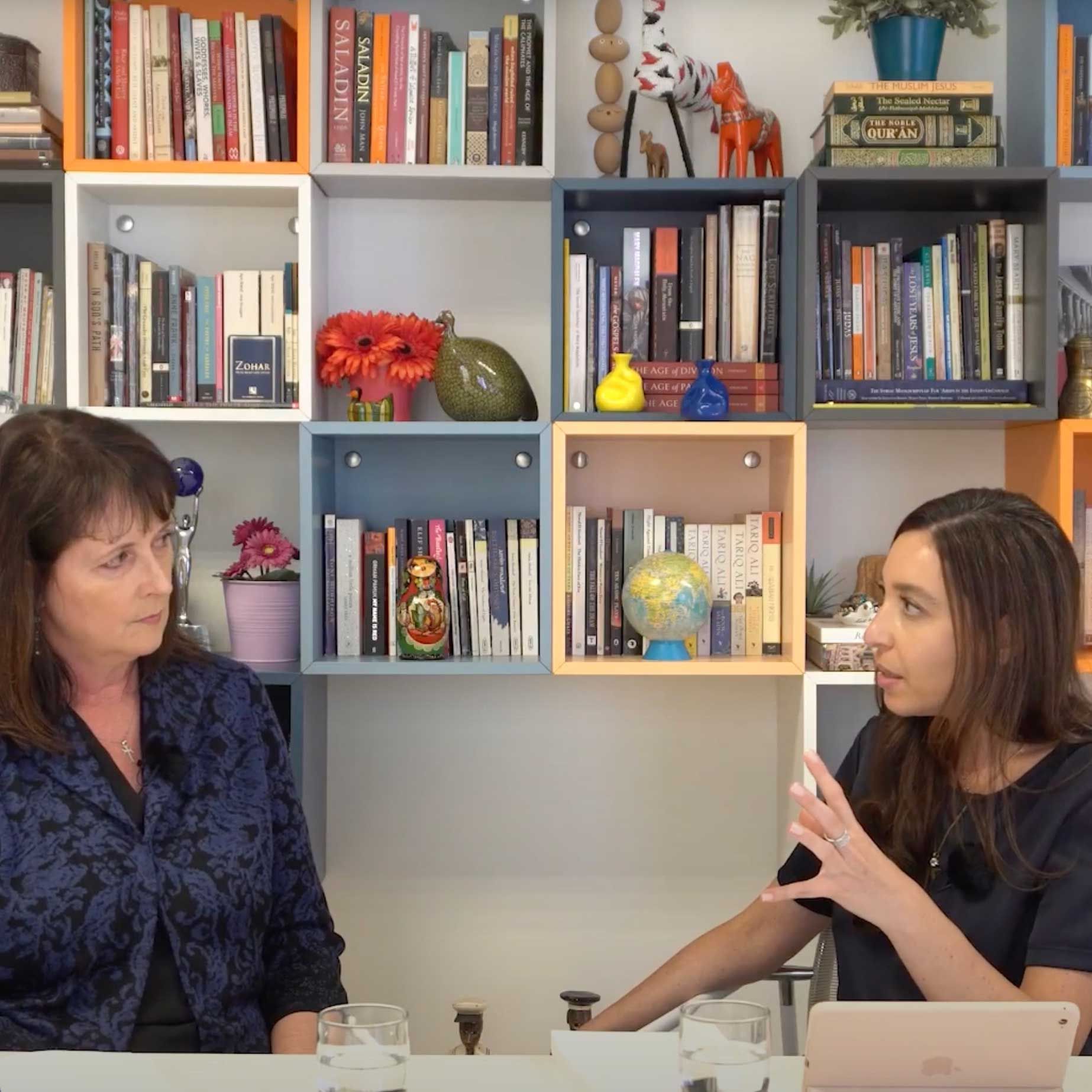 Nadine Maenza and Lynn Zovighian doing a podcast, in front of a bookcase; one gestures, the other listens.