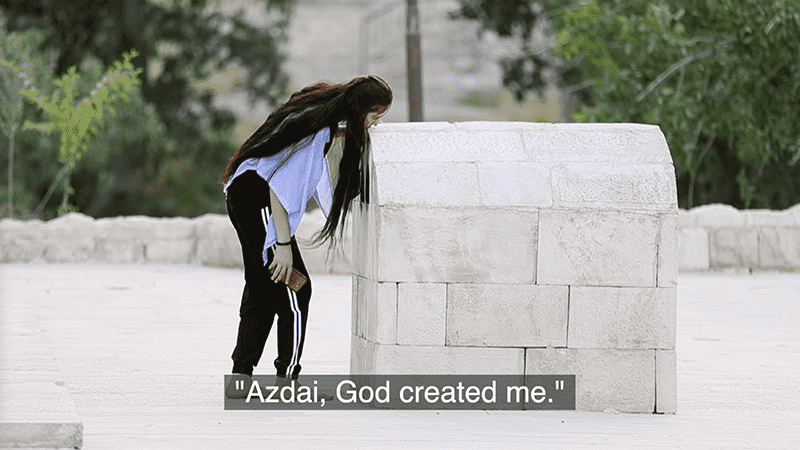 Image showing a woman leaning forward against a stone memorial structure subtitle text reads