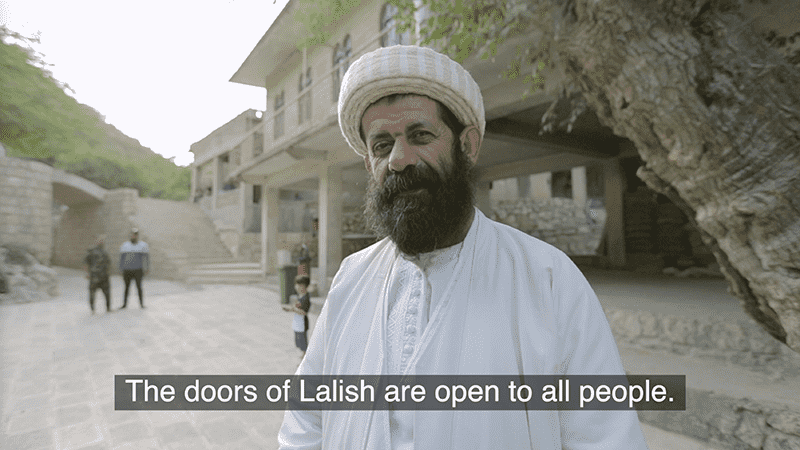 Image showing a man in white robes standing outside a building in Lalish; caption text visible about open doors