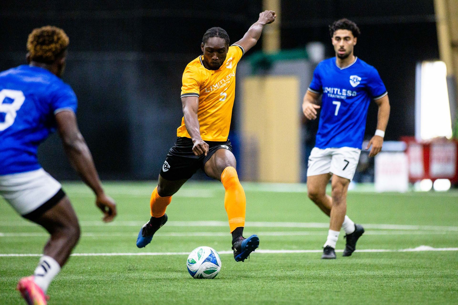 A player from Team Yellow, surrounded by Team blue players, in mid flight winds up to drive the ball on net at the Viktoria Soccer Club indoor field.