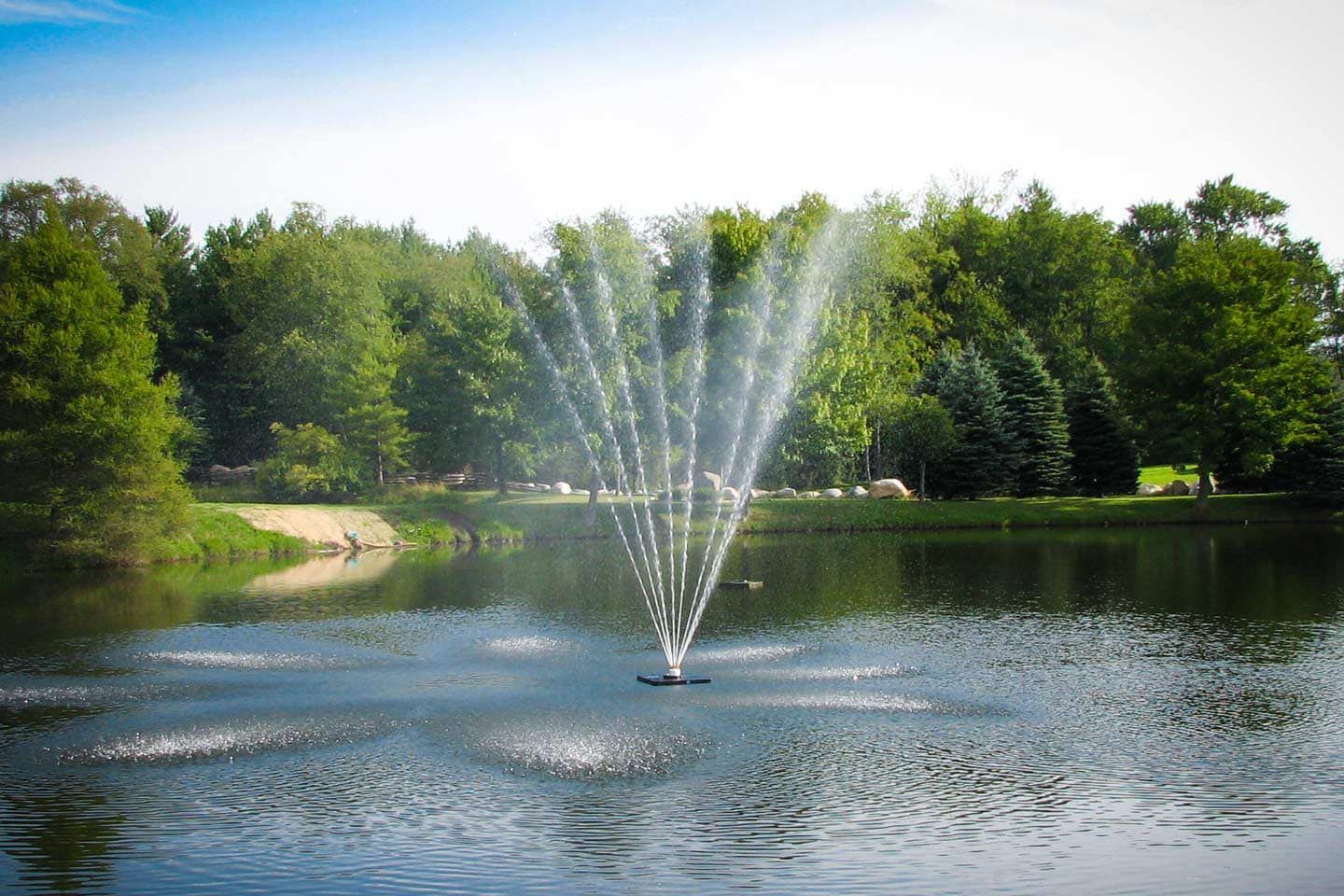 A fountain in the middle of a lake with trees in the background.