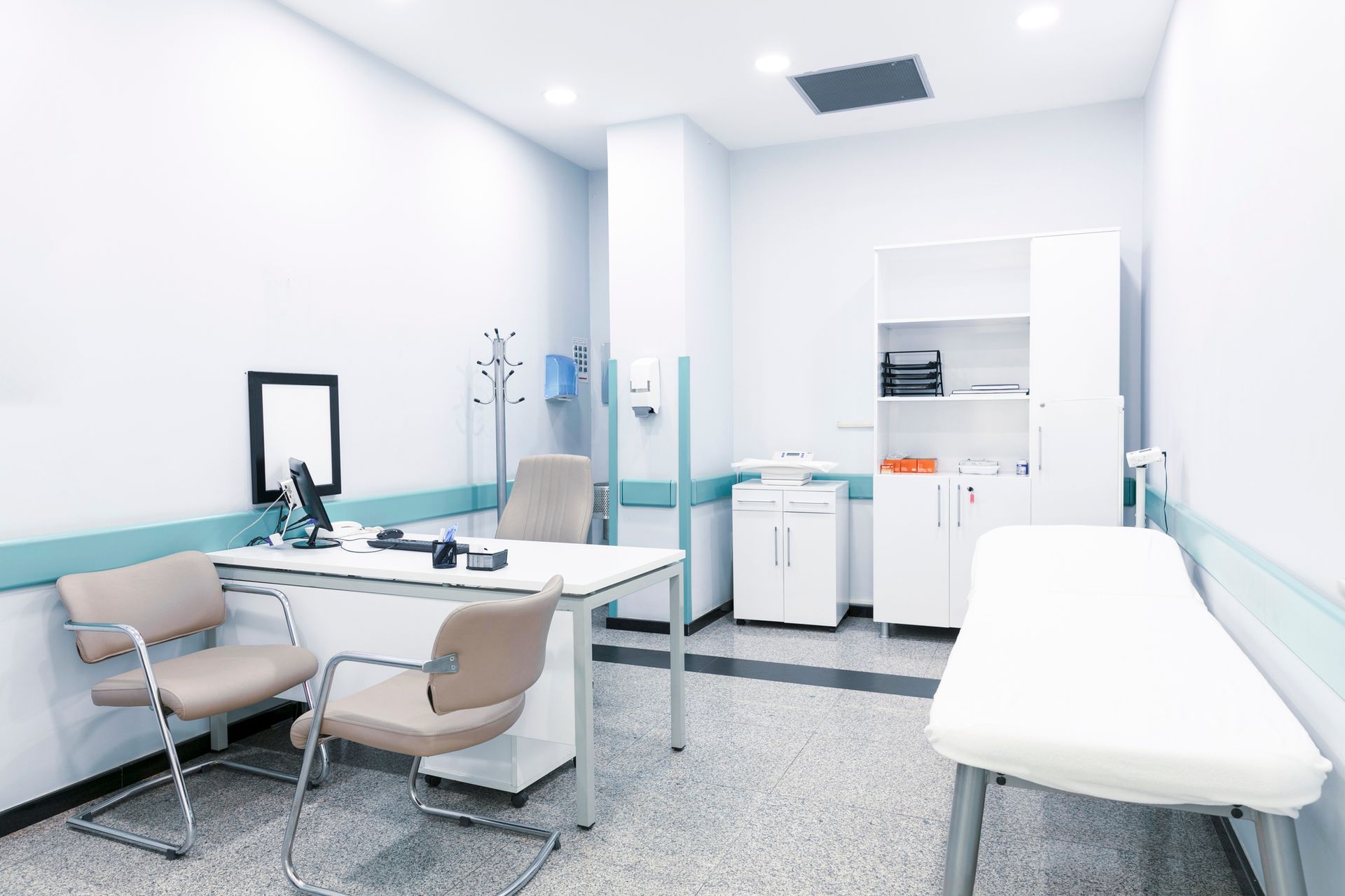 Doctor's office interior with examination table, desk, chairs, and medical equipment.