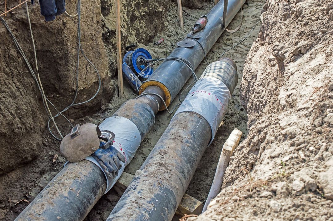 Due grandi tubi industriali giacciono in una trincea di terra, mostrando segni di lavori di installazione in corso.