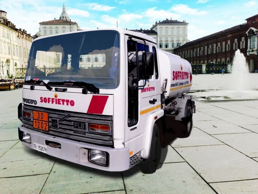 Un'autocisterna bianca della marca Soffietto parcheggiata in una piazza cittadina, di fronte a una fontana e ad alcuni edifici storici.
