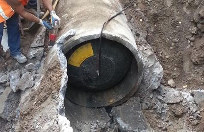 Un operaio con indosso un giubbotto di sicurezza inserisce un tappo gonfiabile in un tubo di cemento all'interno di uno scavo.