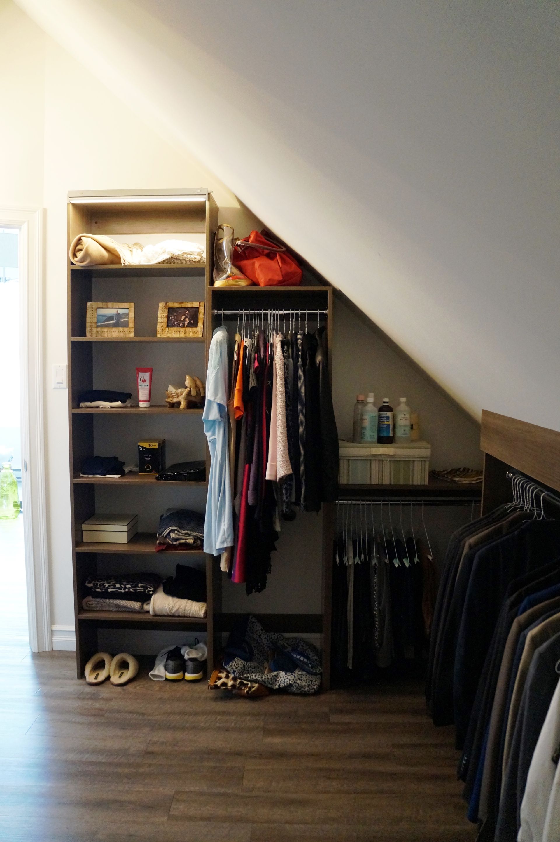 Un placard avec un plafond incliné et des étagères remplies de vêtements et de chaussures.