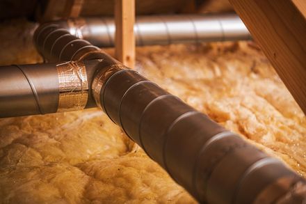 Insulated metal ductwork in an attic above yellow fiberglass insulation