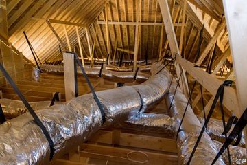 Insulated air ducts running through a wooden attic framing under construction