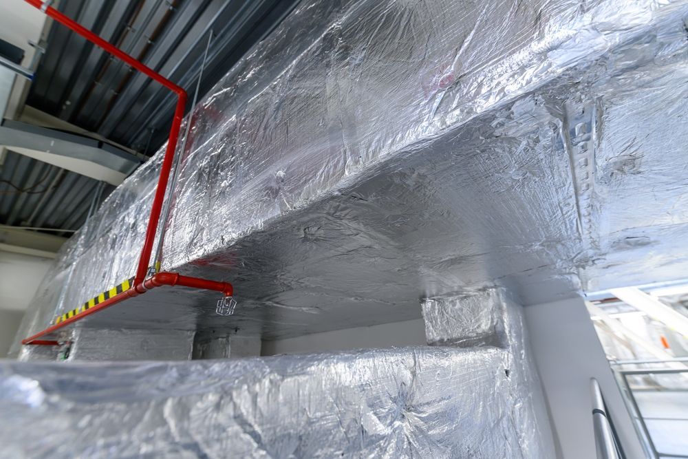Foil-wrapped industrial ductwork with red support brackets in a building interior