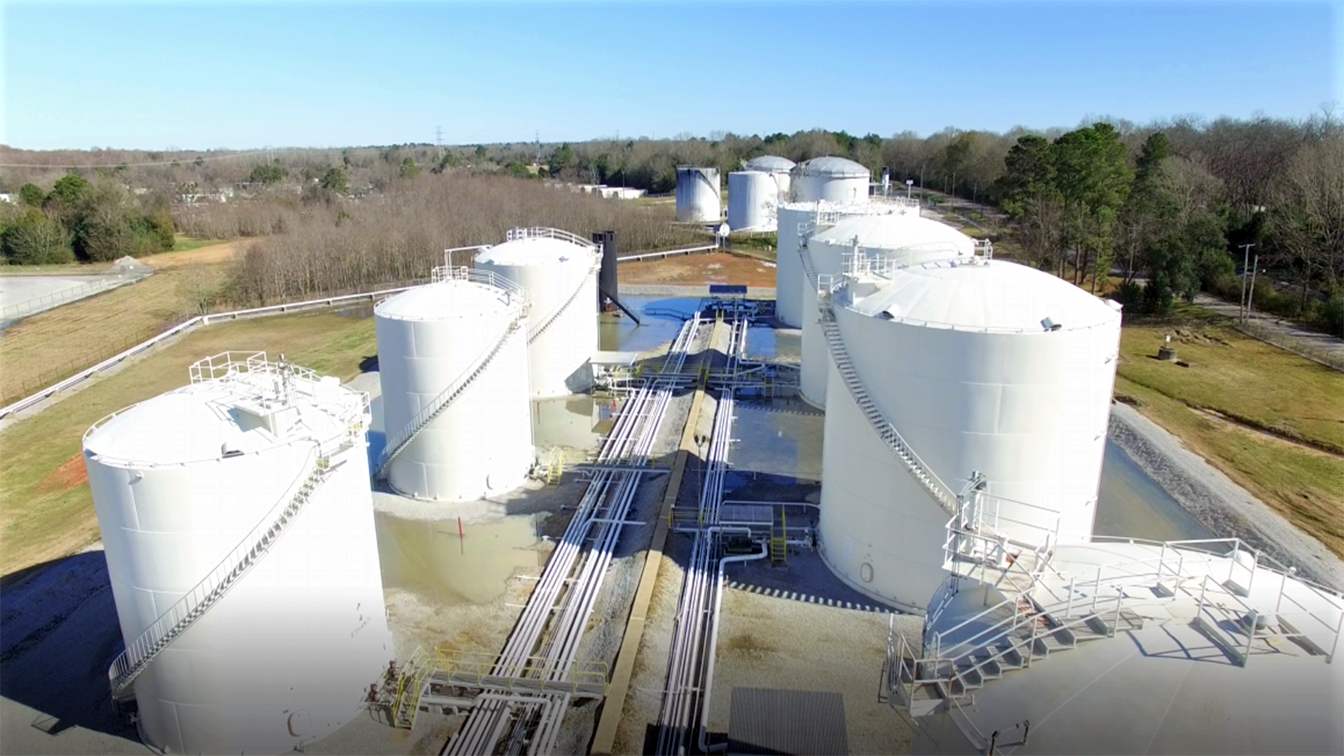 An aerial view of a row of large white tanks in a field.