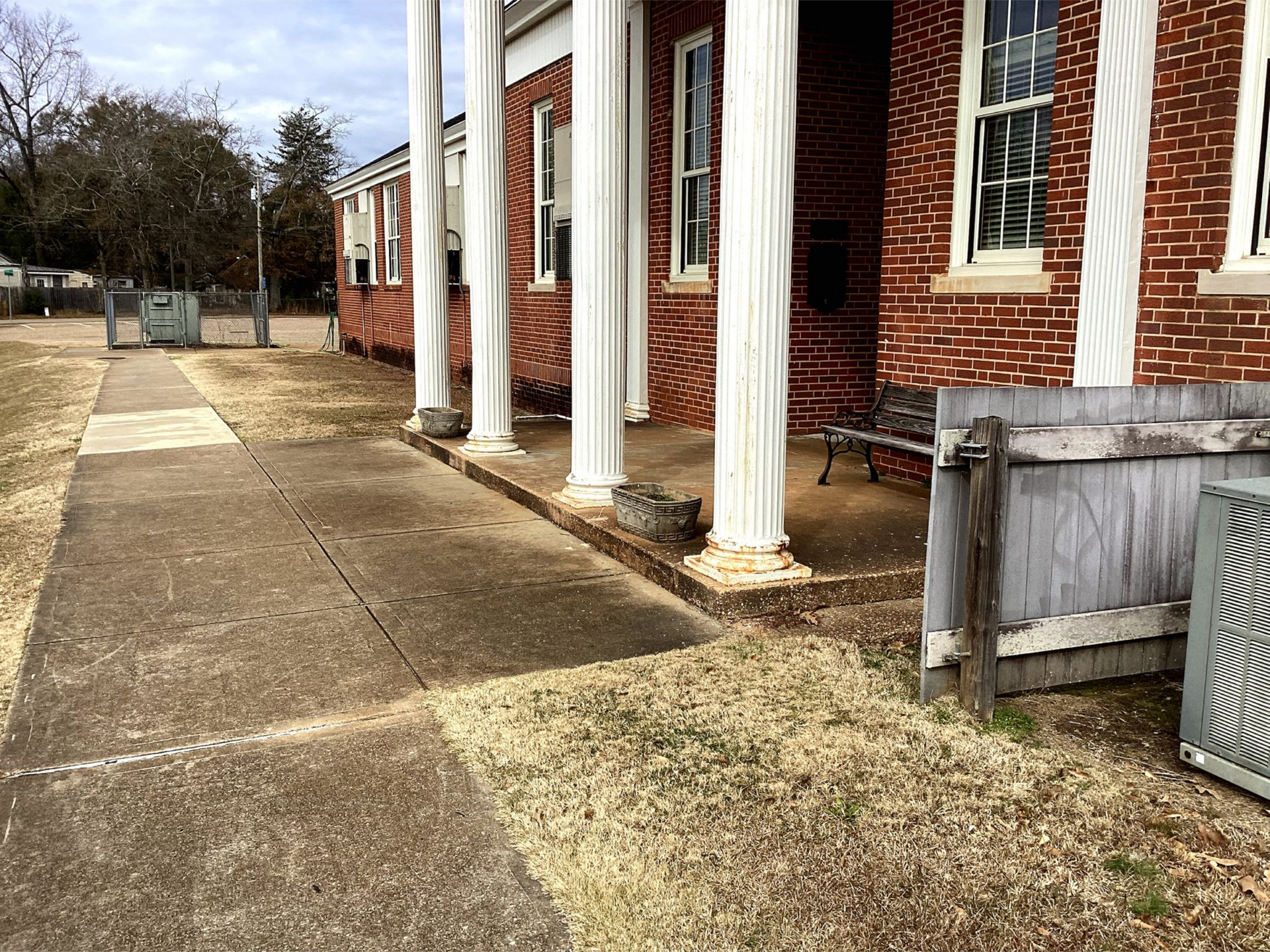 Brick commercial building with white columns, windows, covered entrance, and concrete walkway