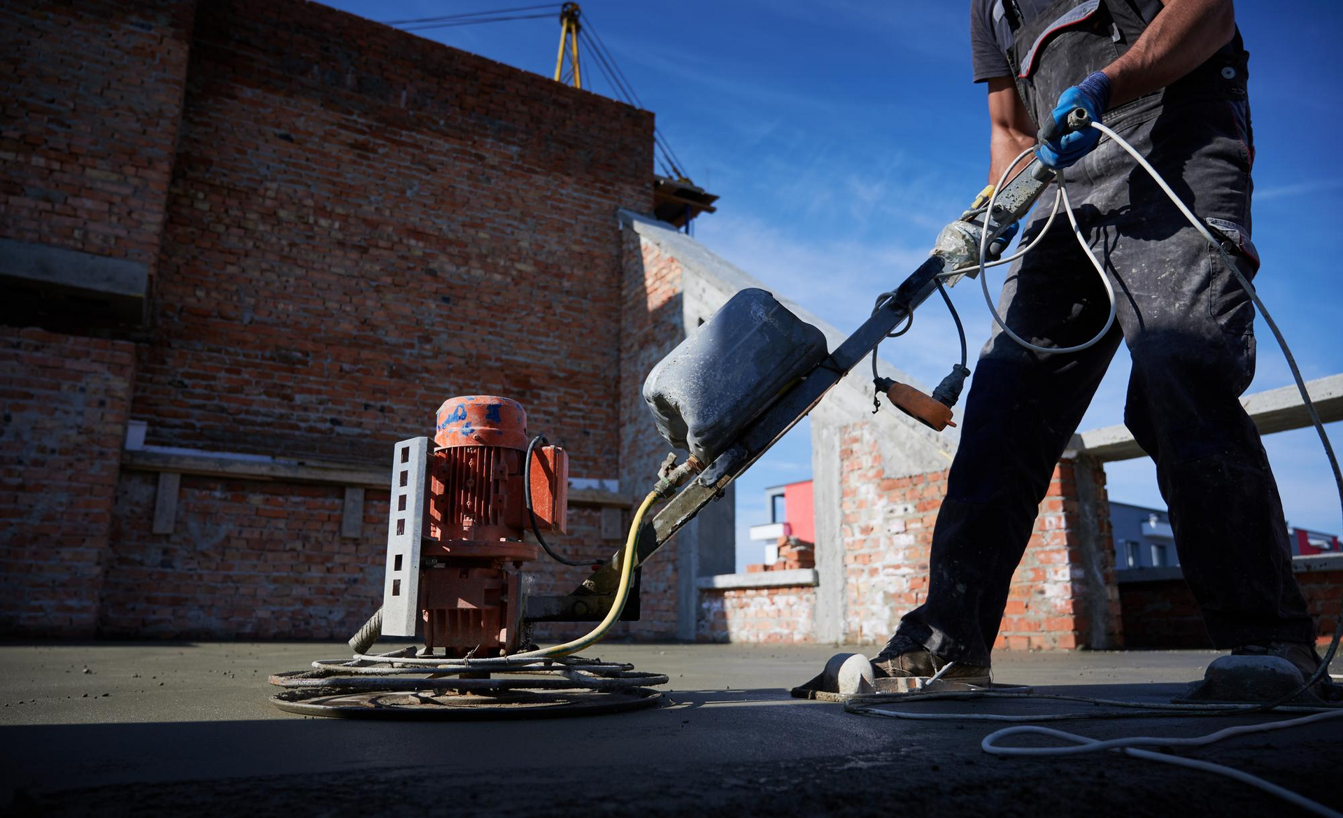 “Construction worker using a power trowel to smooth and finish a freshly poured concrete floor at a 