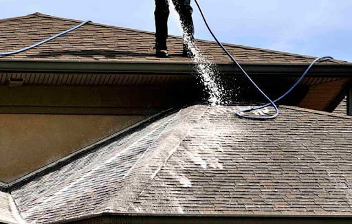 Professional pressure washing a shingle roof to remove dirt and buildup.