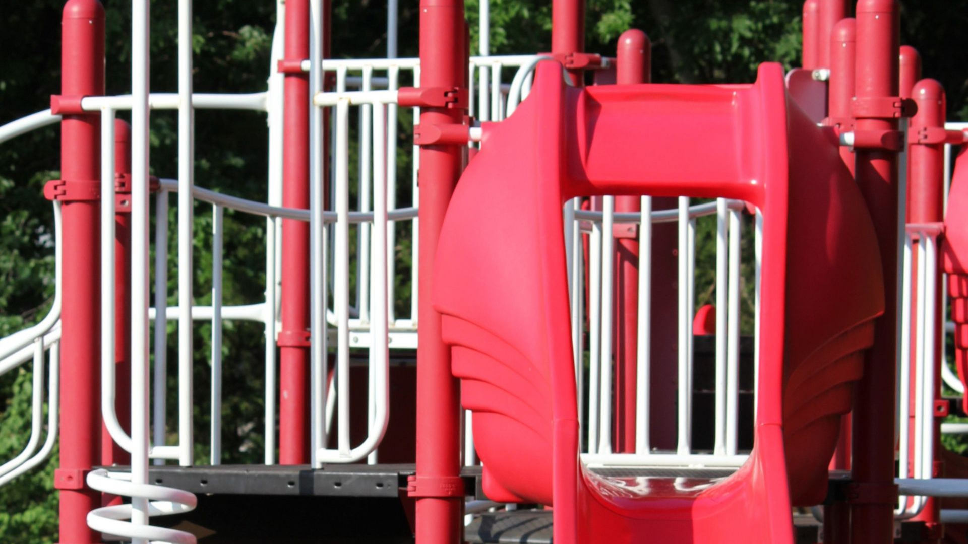 Red playground slide with climbing bars and a spiral ladder on a rubber play surface