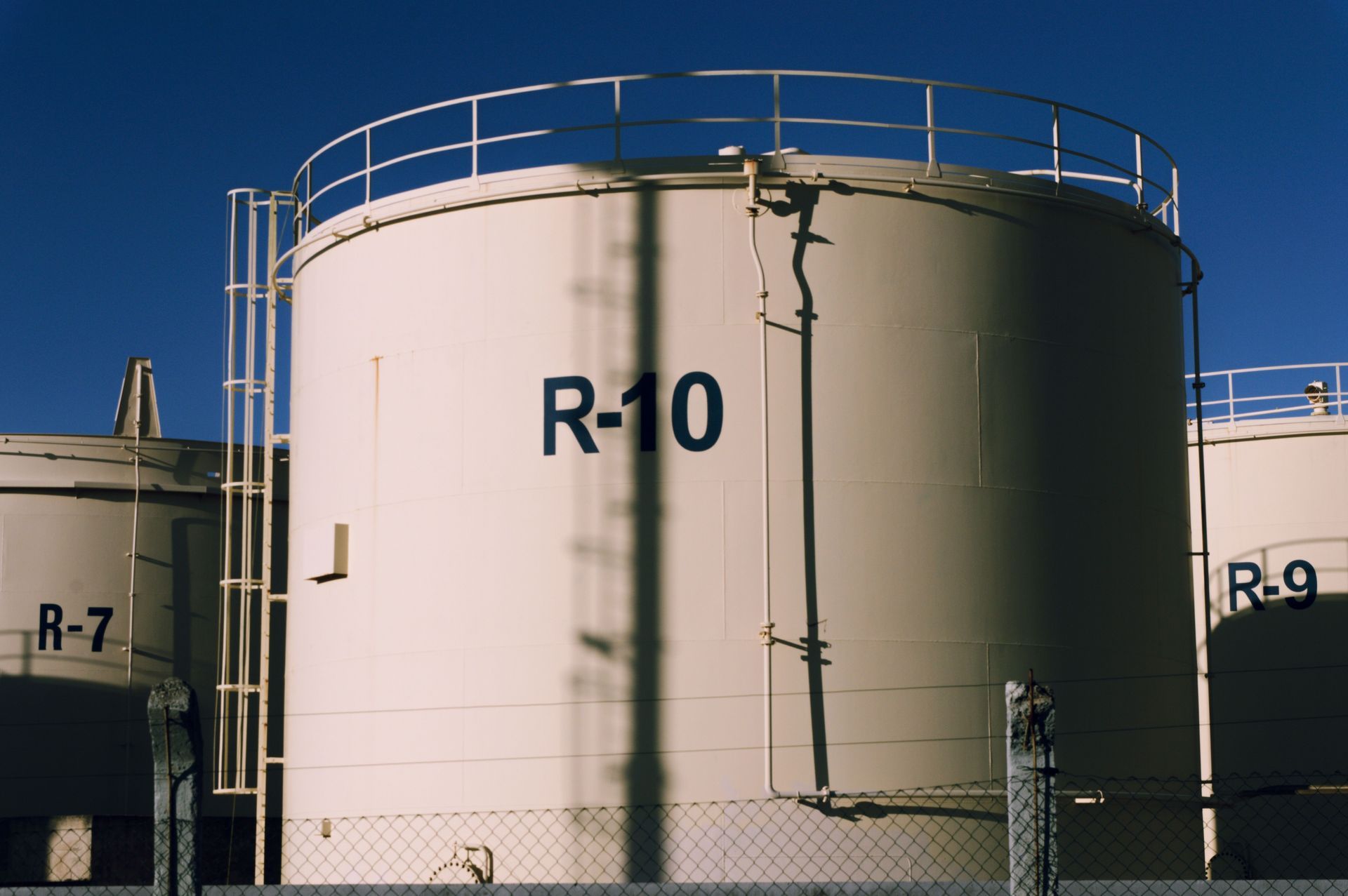 Large white industrial storage tank labeled R-10 beside smaller tanks under a clear blue sky