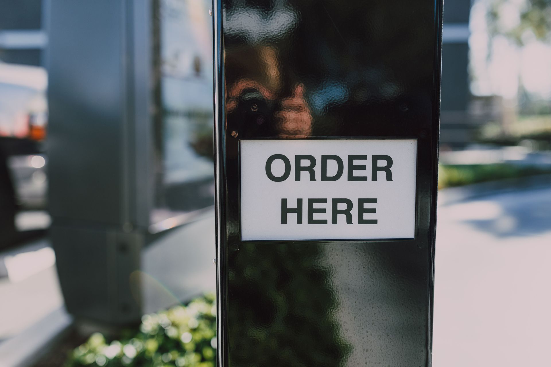 Drive-thru sign reading “ORDER HERE” on a black post beside a window