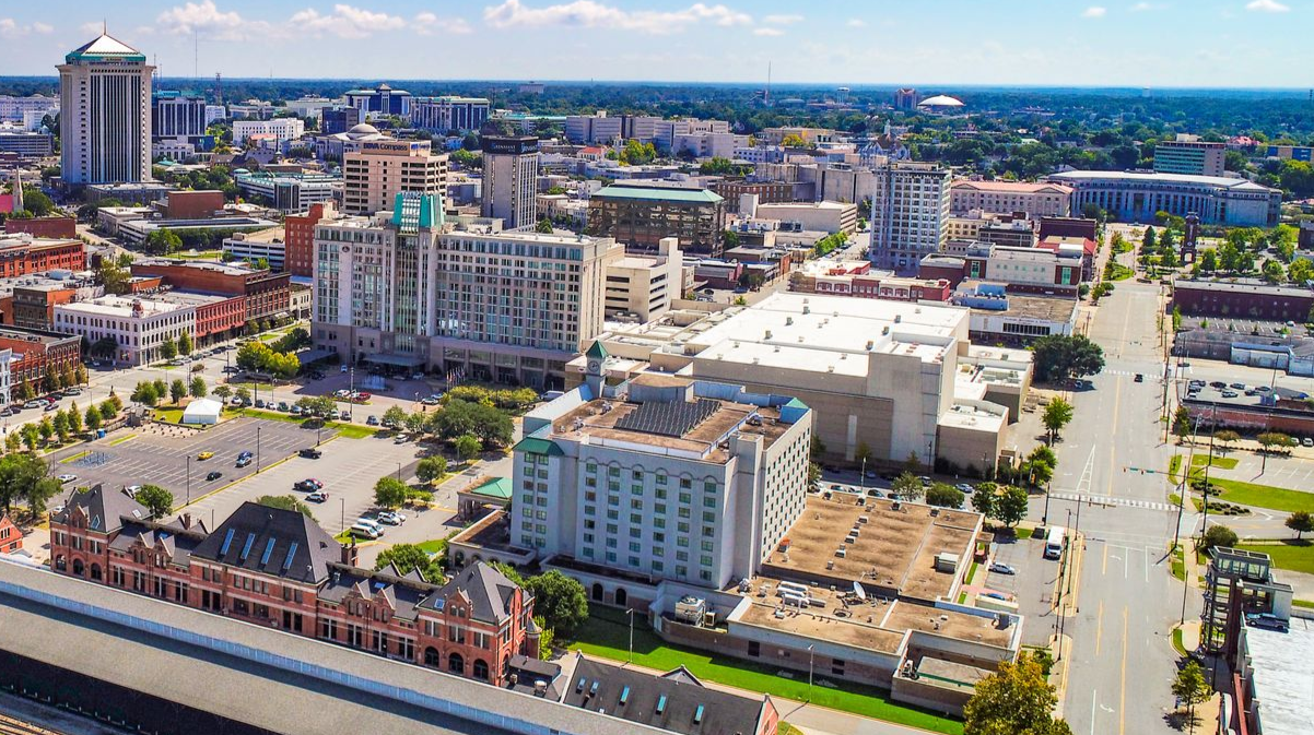 Aerial view of Montgomery, Alabama downtown with tall buildings, a historic train station, and blue sky.