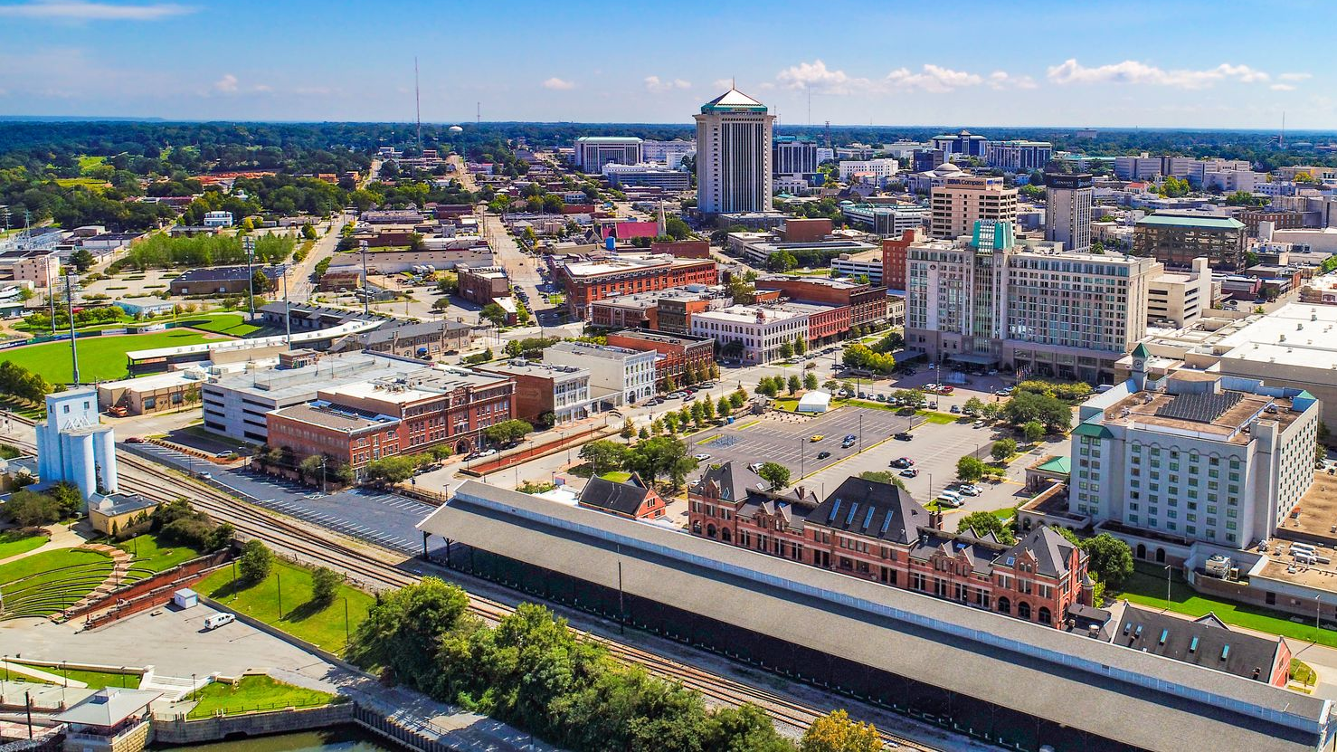 An aerial view of a downtown cityscape featuring a prominent tall round tower, historic brick buildings, and urban parks.