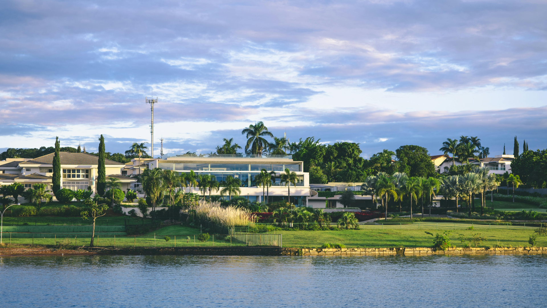 Wide riverfront view of houses and trees under a cloudy blue sky at dusk