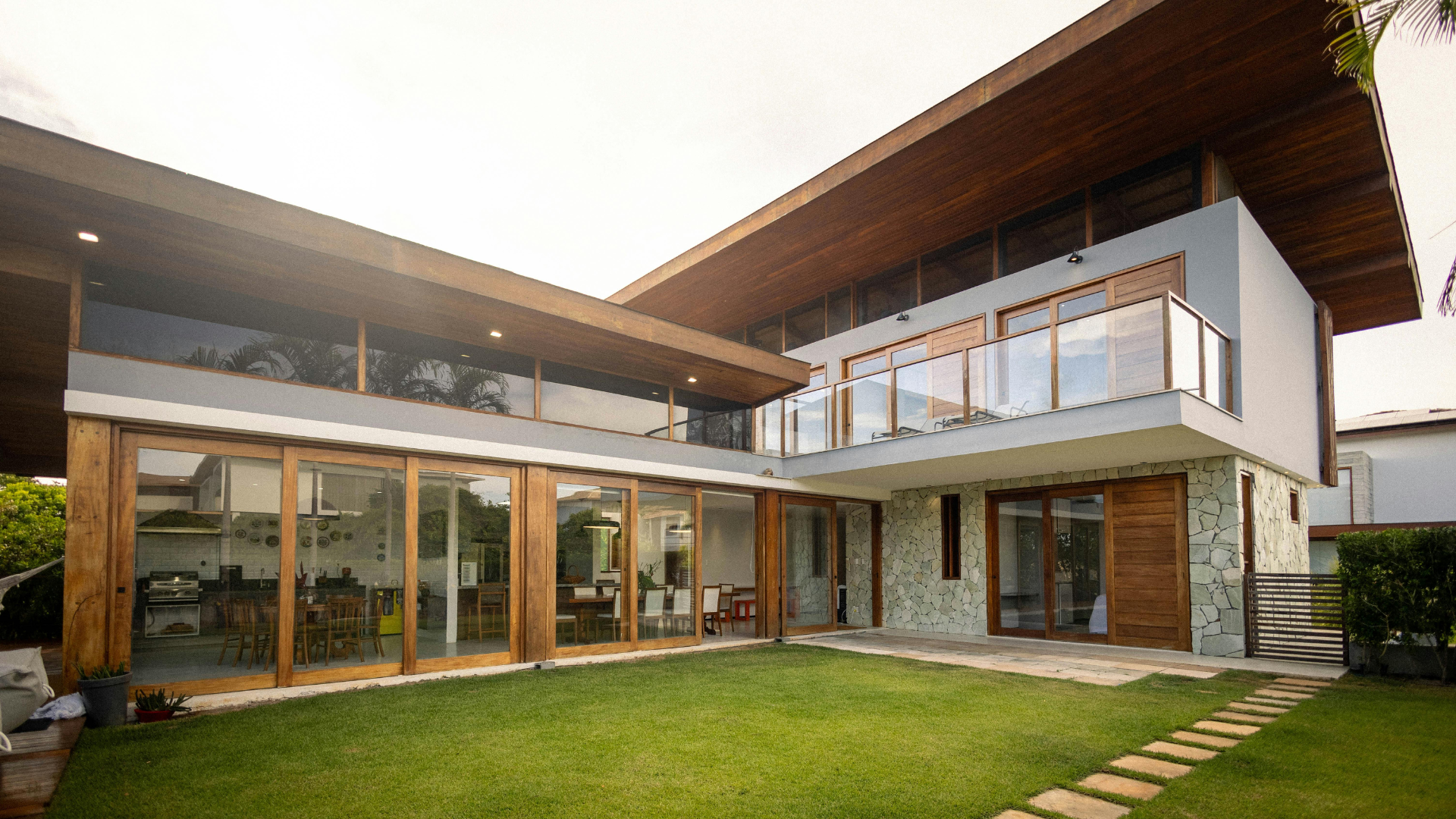 Modern two-story house with large glass walls, wooden roof, and a green lawn