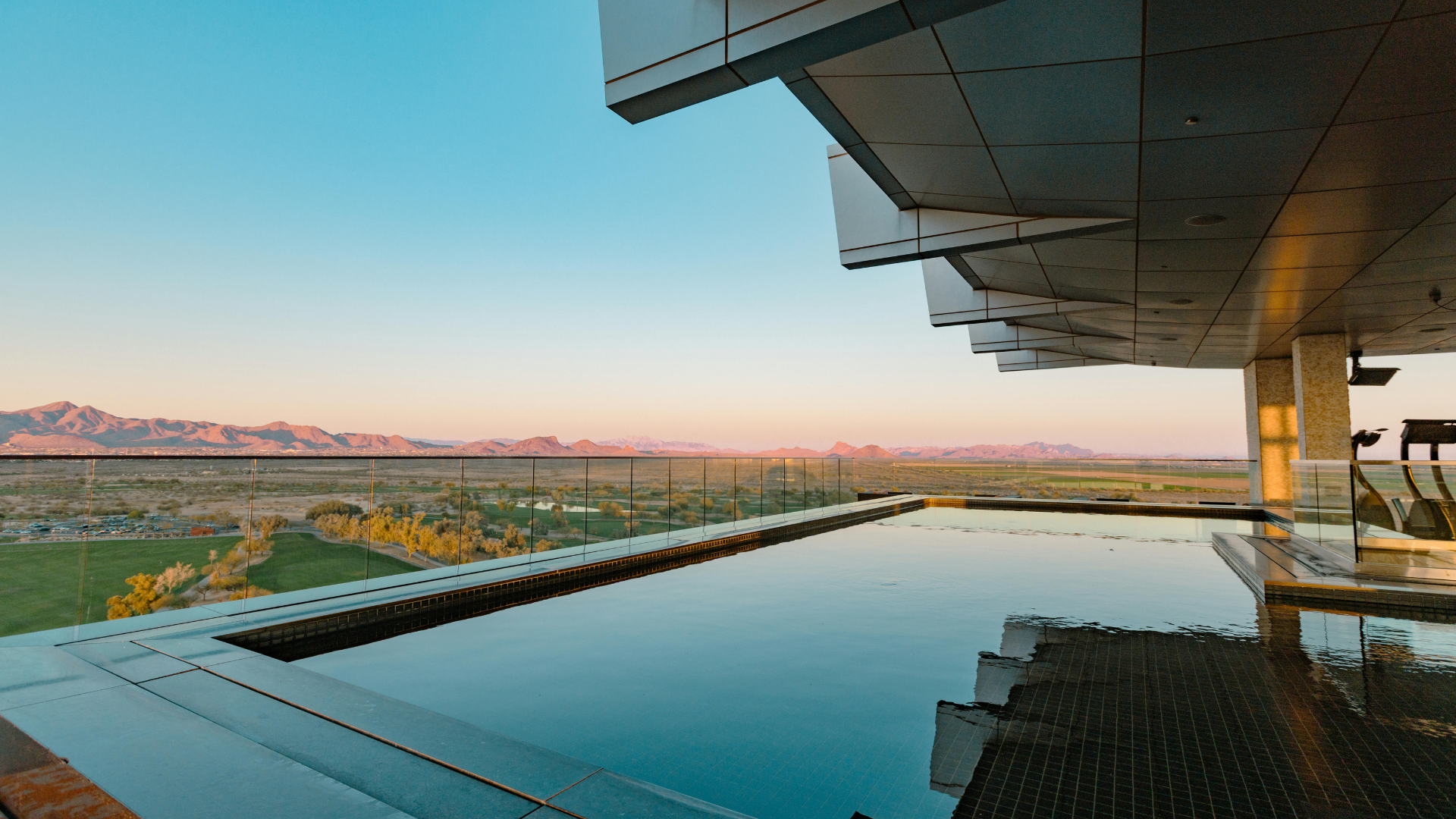 Modern infinity pool beside a luxury terrace at sunset, overlooking mountains and water