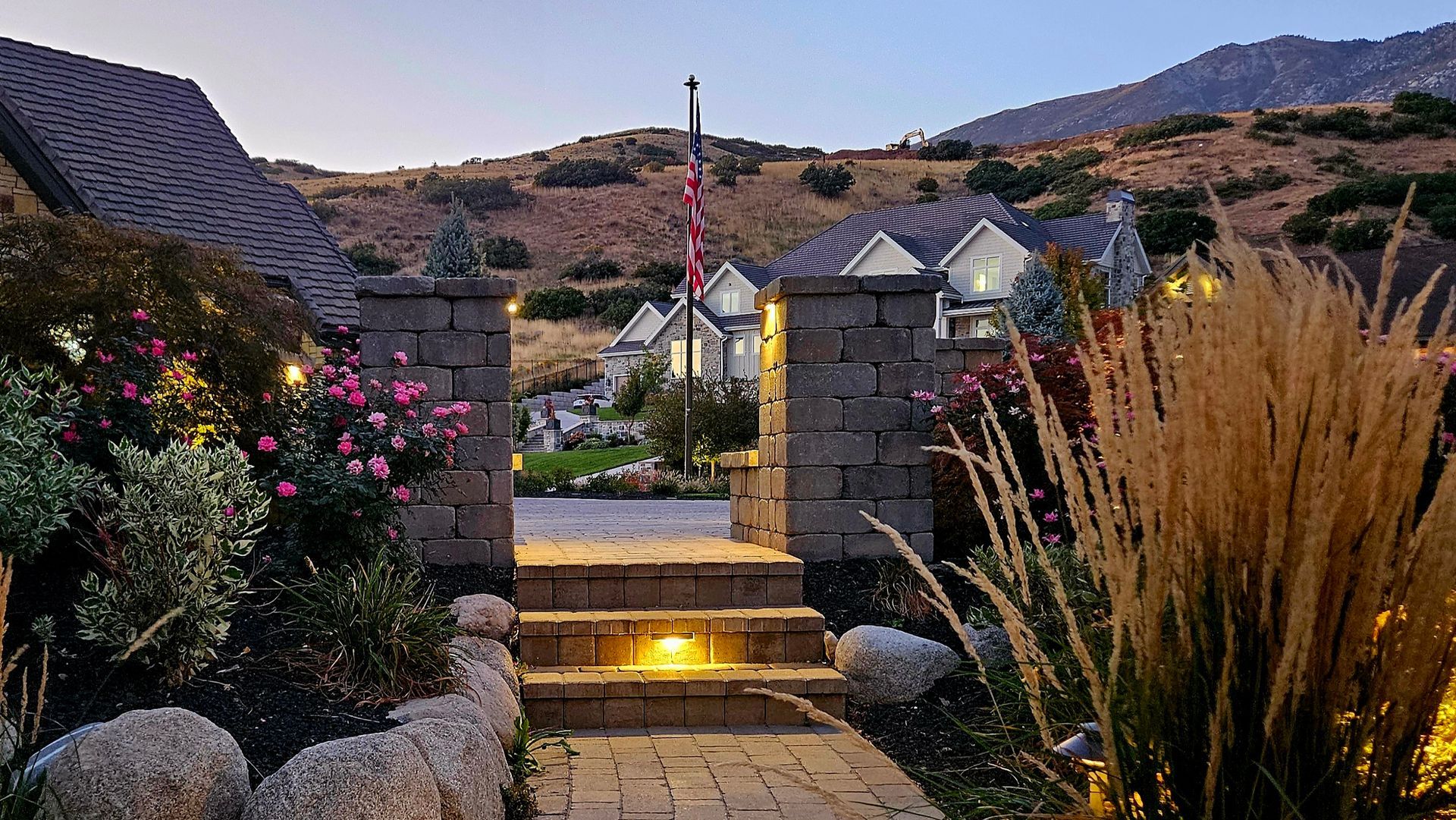 A stone patio with a rectangular swimming pool, a water feature, a waterslide tunnel, and tiered landscaping.