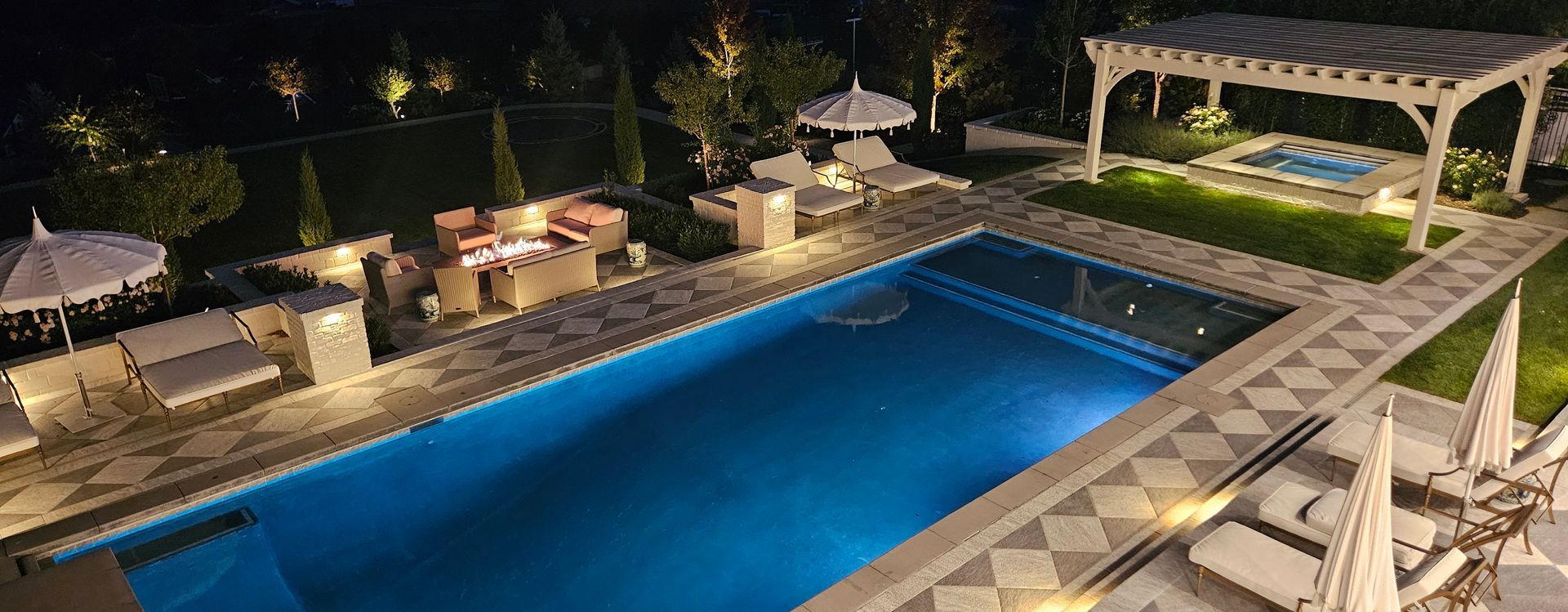 A stone patio with a rectangular swimming pool, a water feature, a waterslide tunnel, and tiered landscaping.