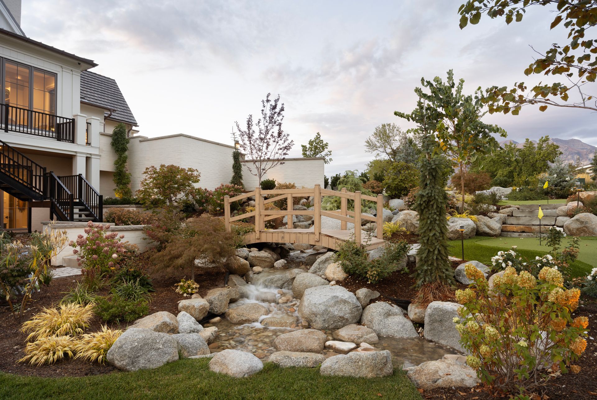 A stone patio with a rectangular swimming pool, a water feature, a waterslide tunnel, and tiered landscaping.