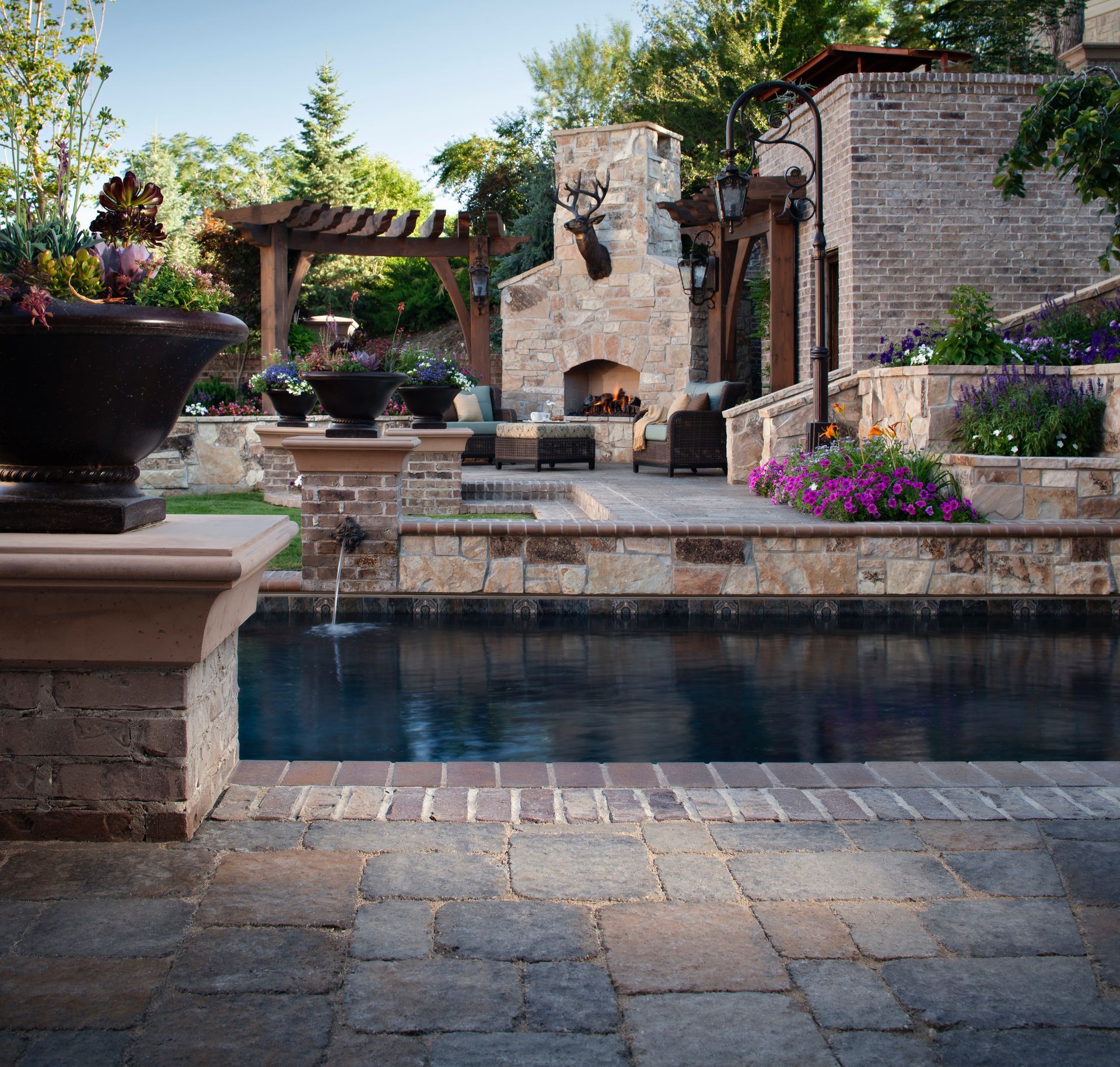 A tiered stone garden with a cascading waterfall, stone steps, and colorful flowers along a landscaped pathway.