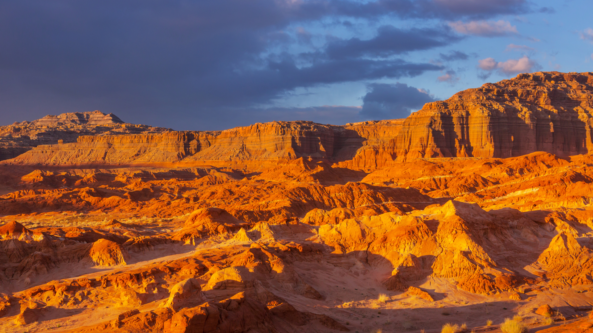 Orange desert mesas and rocky cliffs under a cloudy sky at sunset
