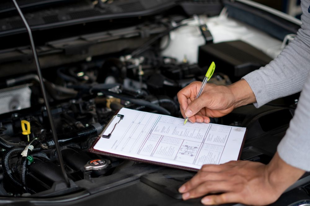 A Person is Writing on a Clipboard in Front of a Car Engine — Ballina Automatics in Ballina, NSW