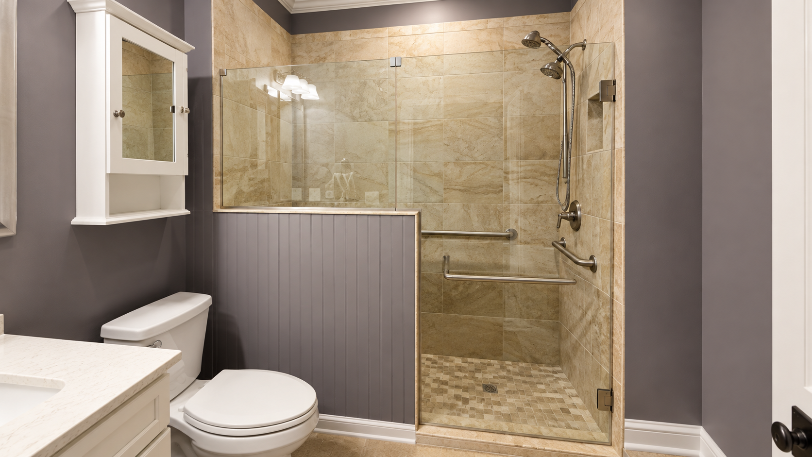 Bathroom with toilet, glass walk-in shower, and beige stone tile backsplash and floor.