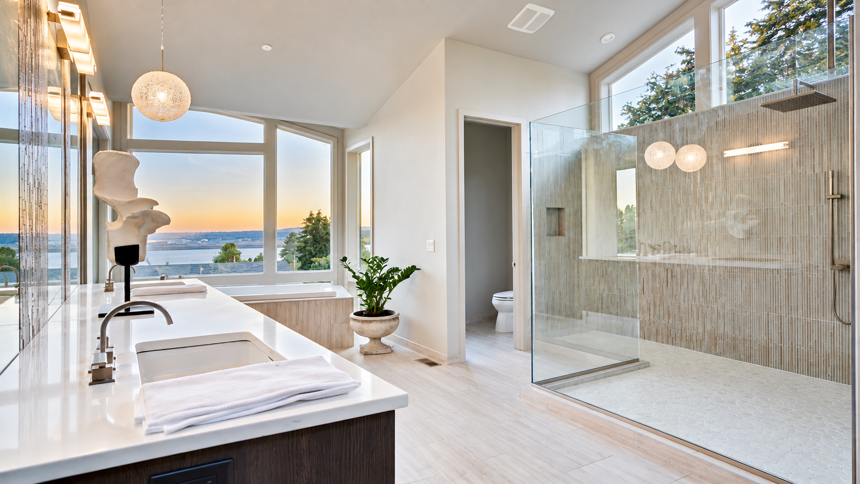 Bright modern bathroom with a soaking tub, glass shower, and large windows overlooking water.