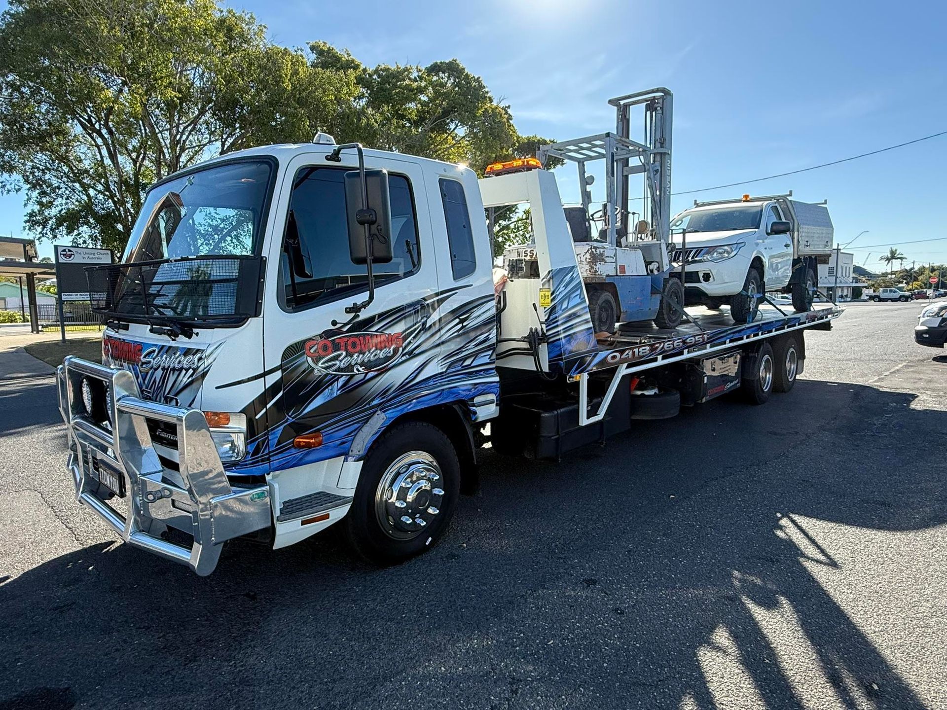 Black Tow Truck Towing a White Vehicle on A Dirt Lot Under a Cloudy Sky — Cq Towing Services In Rockhampton City, QLD