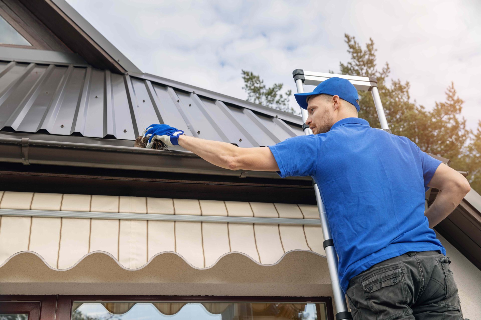 A man is standing on a ladder working on the roof of a house