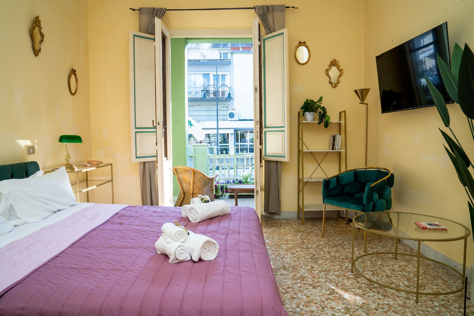 Bedroom with balcony. Purple bedspread, green chair, gold accents, and a small balcony with a view.