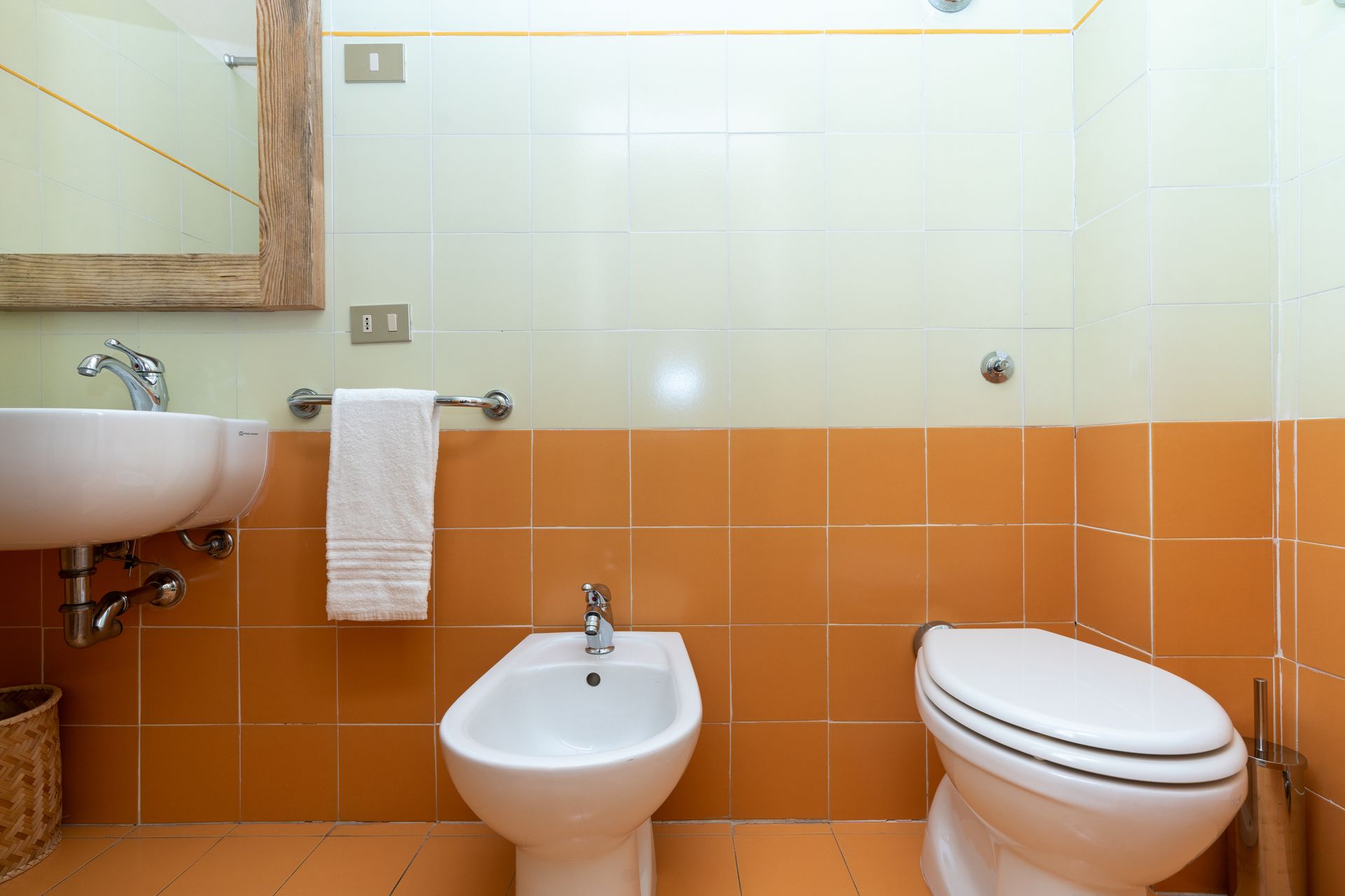 Bathroom with sink, towel, bidet, and toilet. Orange and beige tiles, mirror.