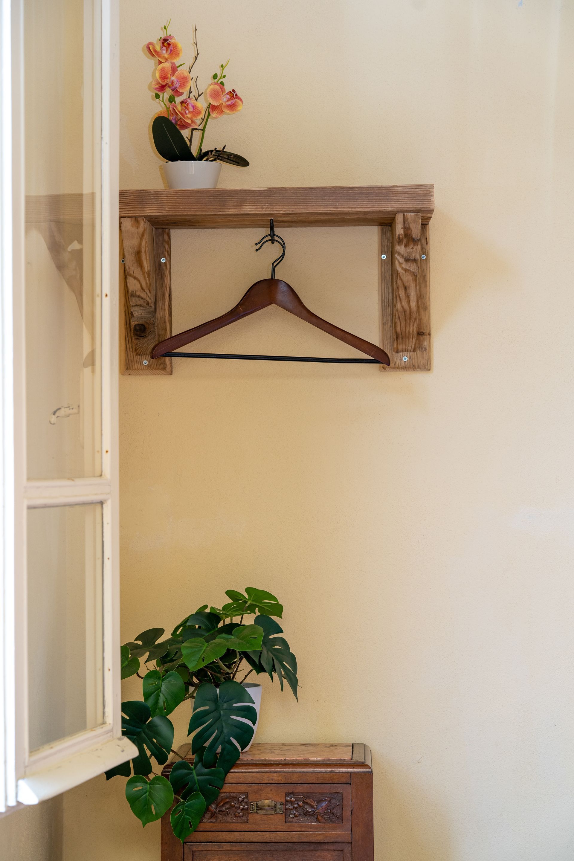 Wooden shelf with a hanger, flower pot, and a leafy plant next to a window.