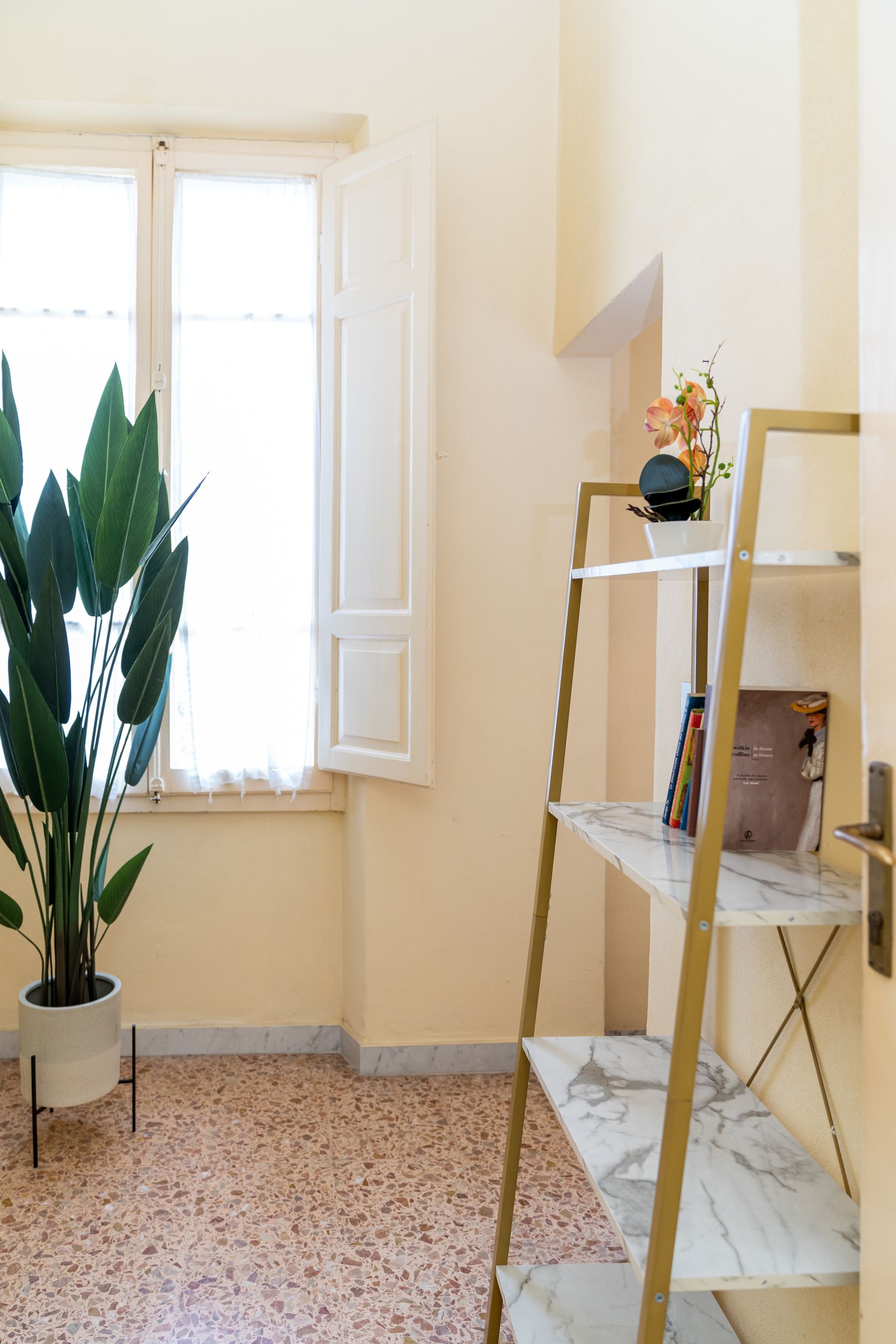 Corner room with window, plant, and gold ladder shelf with decor.