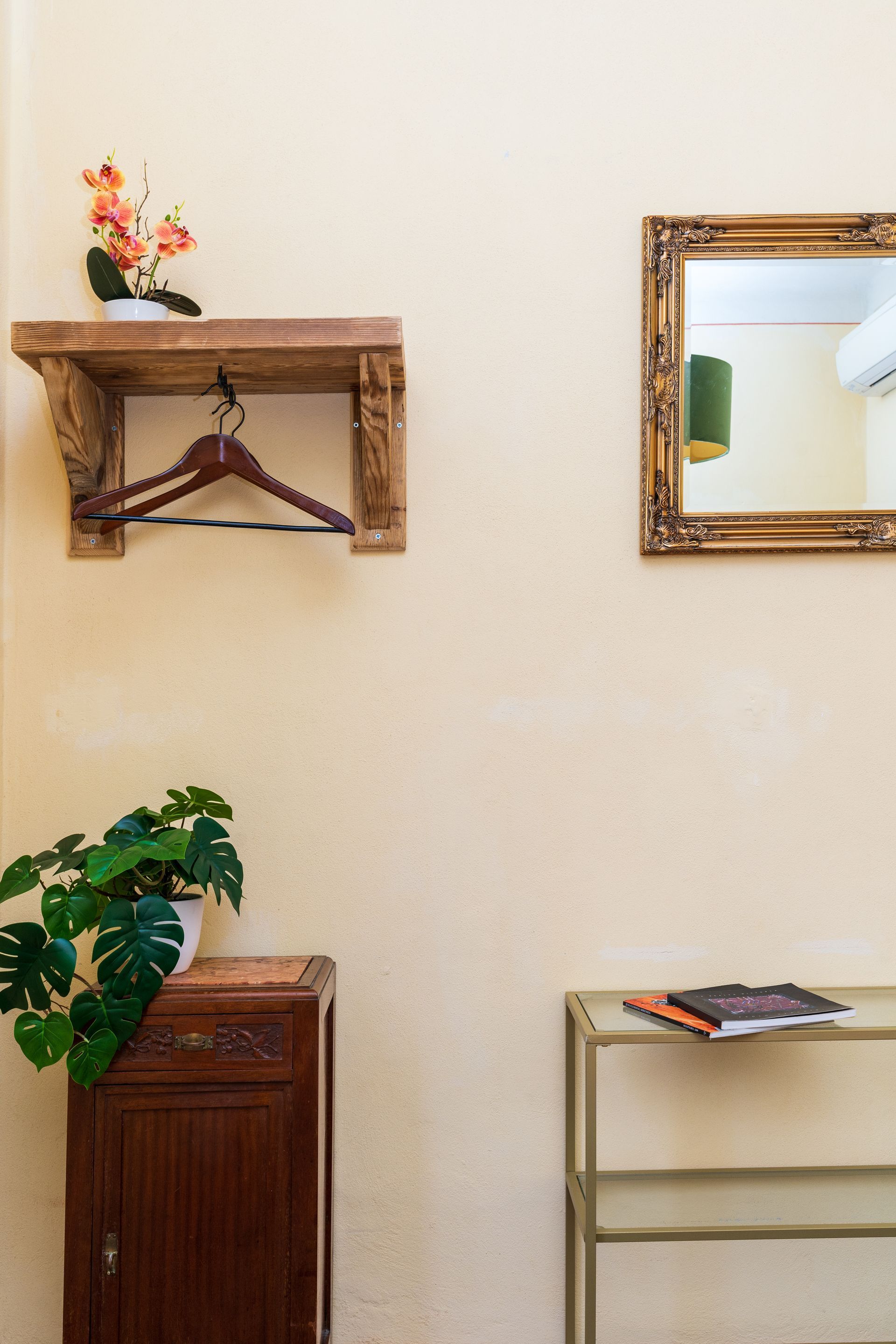 Wooden shelf with hanger, mirror, cabinet with plant, and simple shelf against a cream-colored wall.