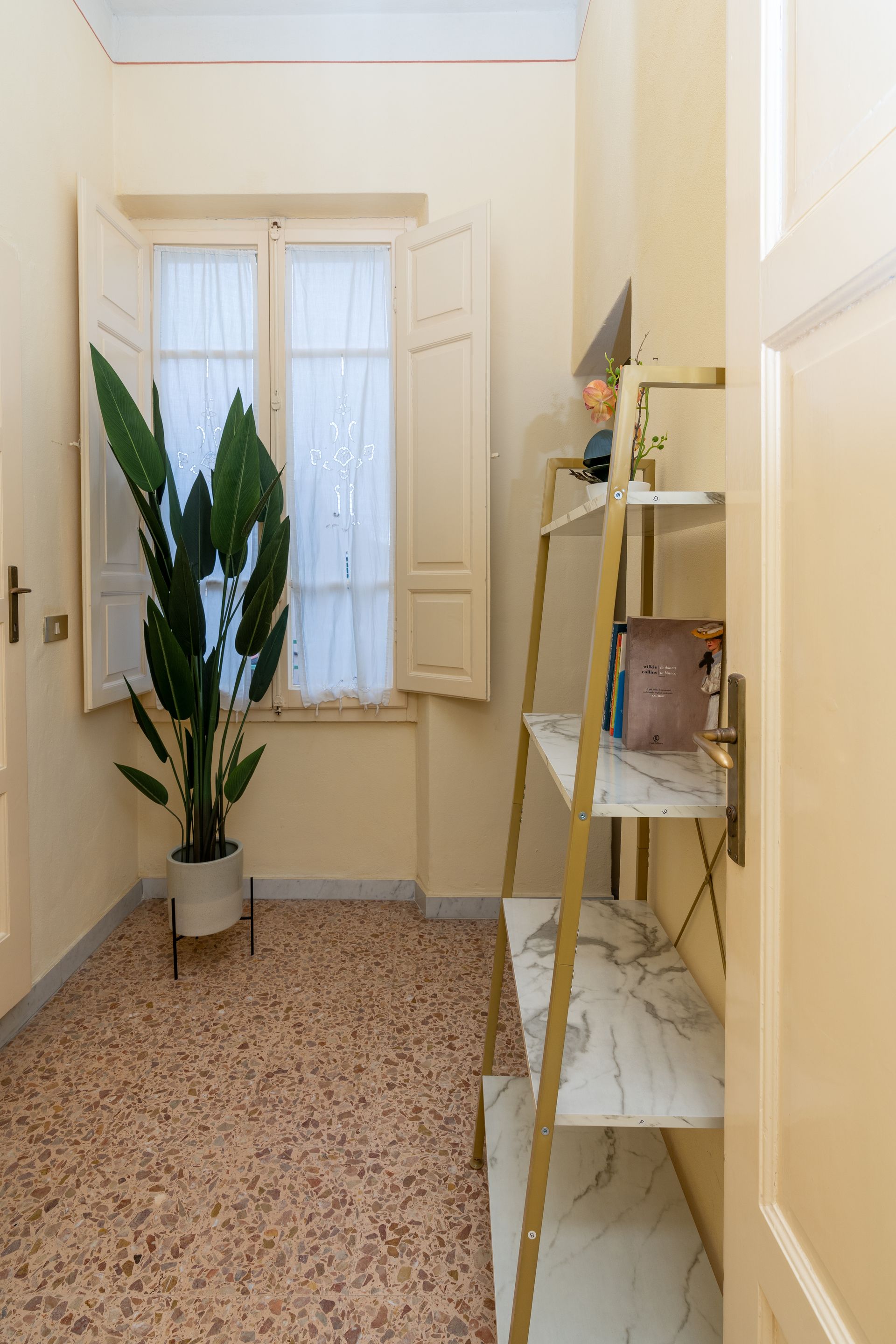 Corner room with window, plant, and shelving unit. Light walls, patterned tile floor, and open door.