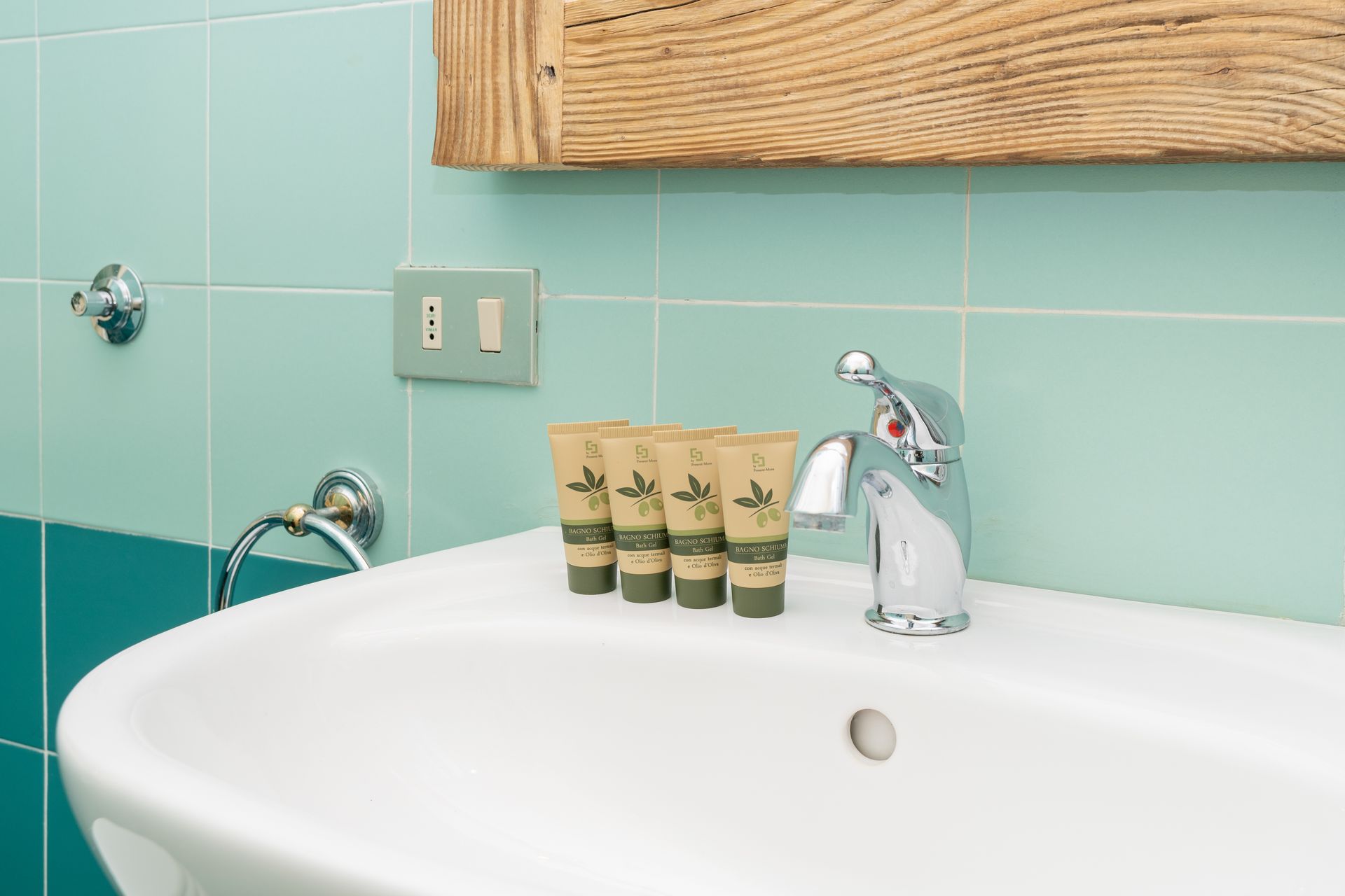 Bathroom sink with turquoise tile, toiletries, and a wooden framed mirror.
