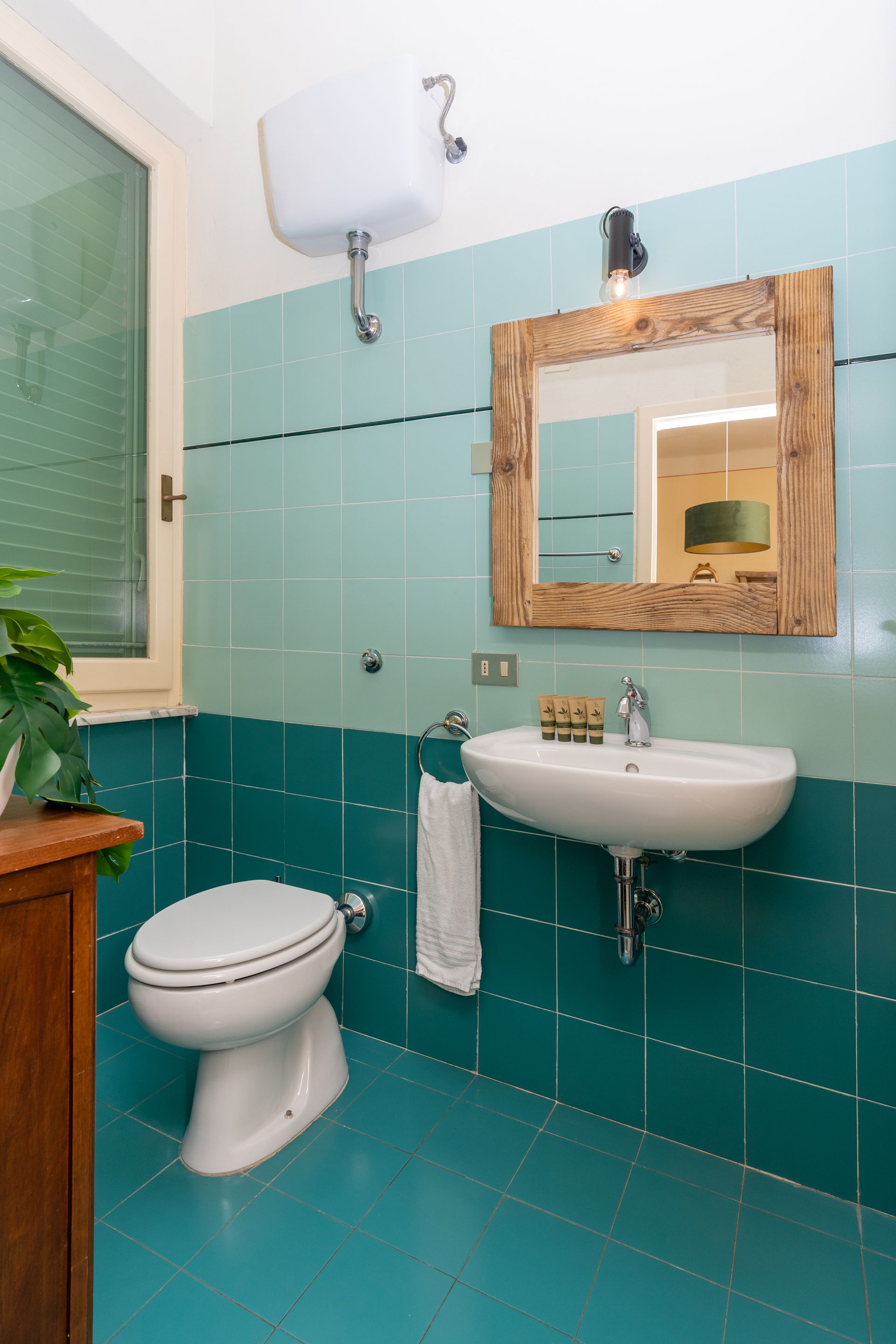 Bathroom with teal tiles, white toilet and sink, wooden mirror frame.