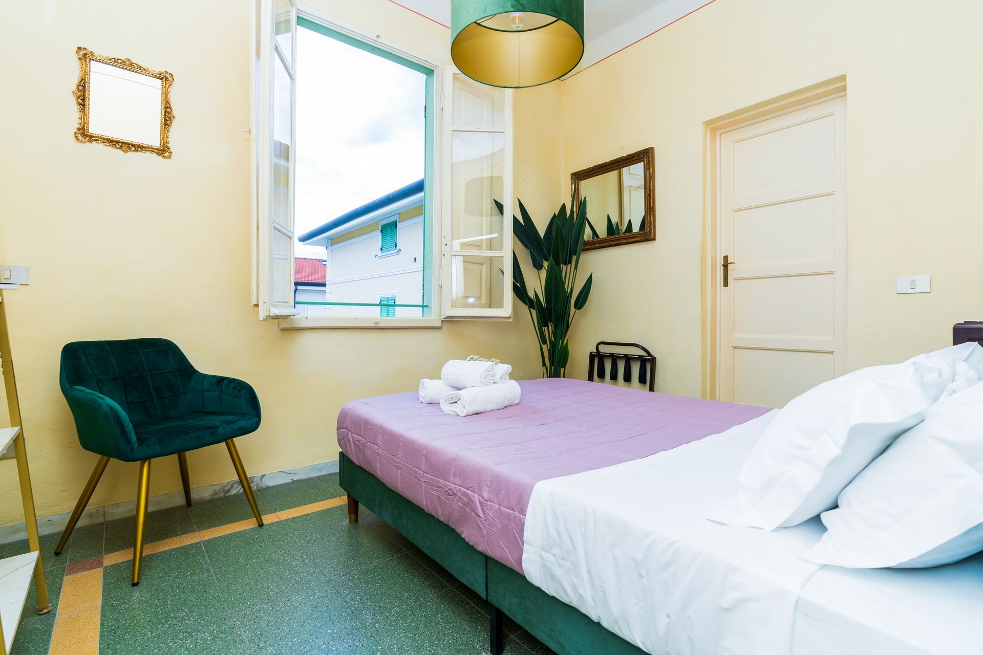 Bedroom with bed, chair, and open window. Green, gold, and pink decor.