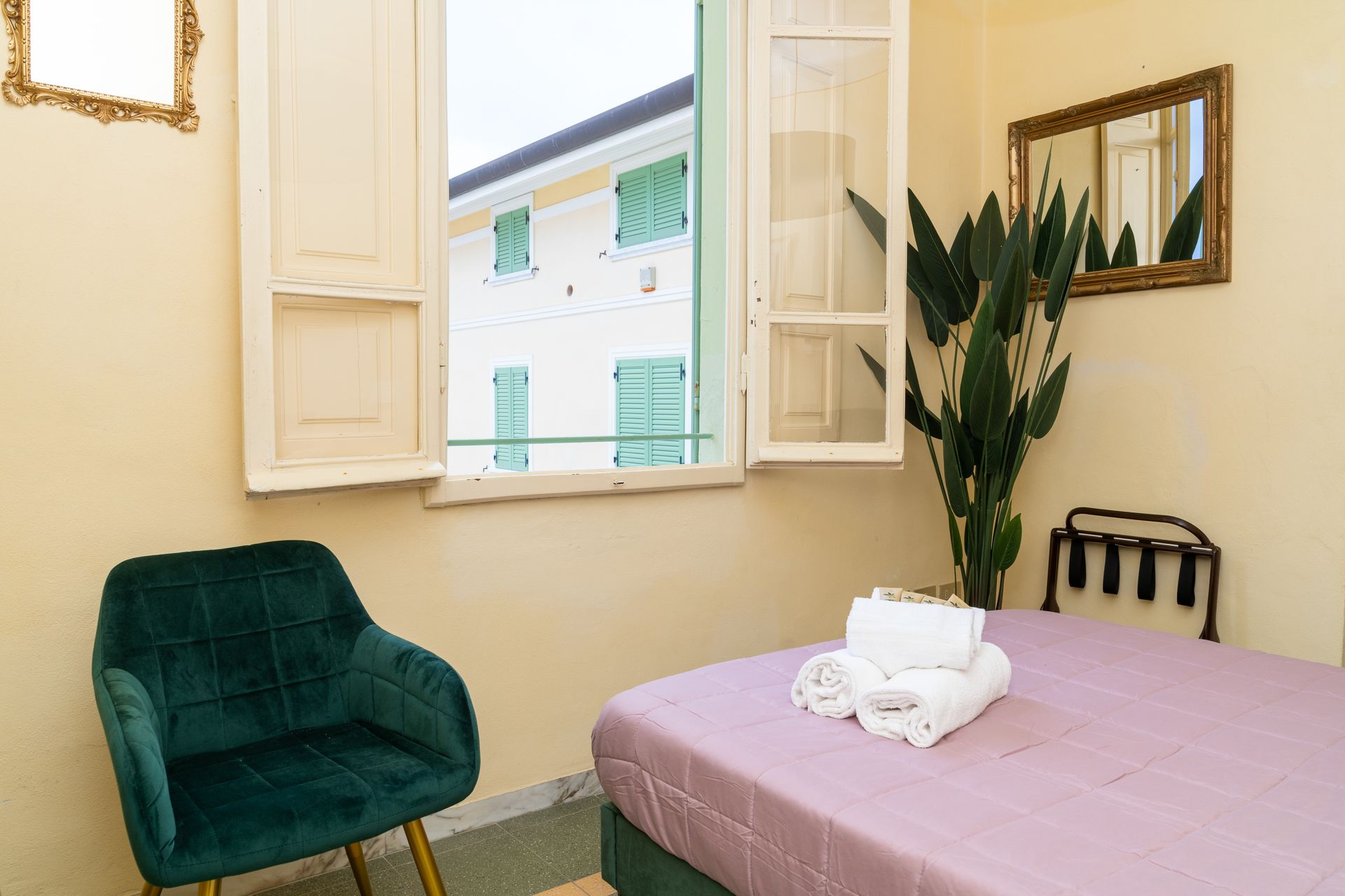 Bedroom with bed, chair, and window overlooking a building. Green and gold accents.