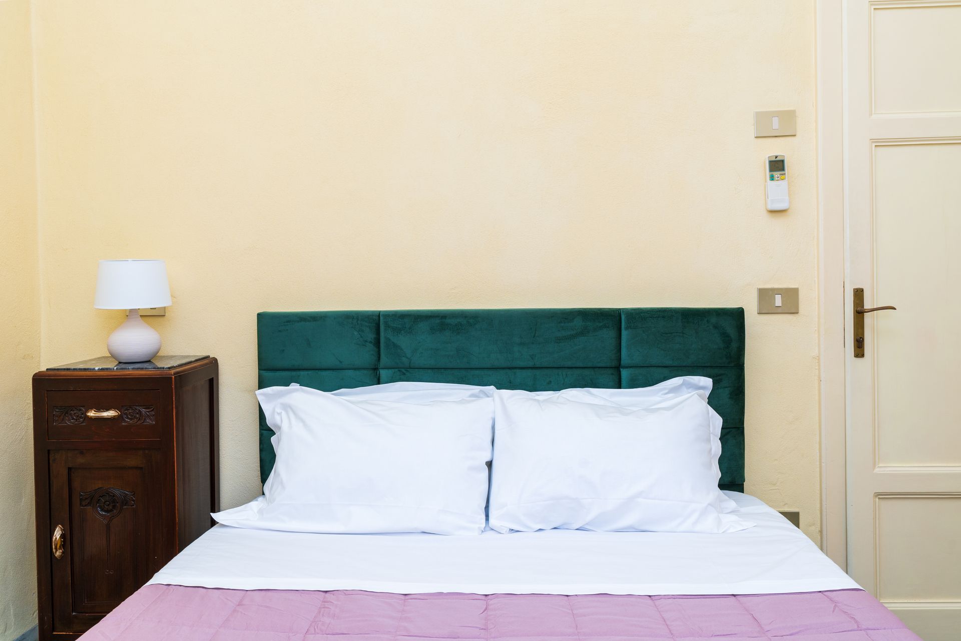 Bedroom with a made bed, nightstand with lamp, and closed door.
