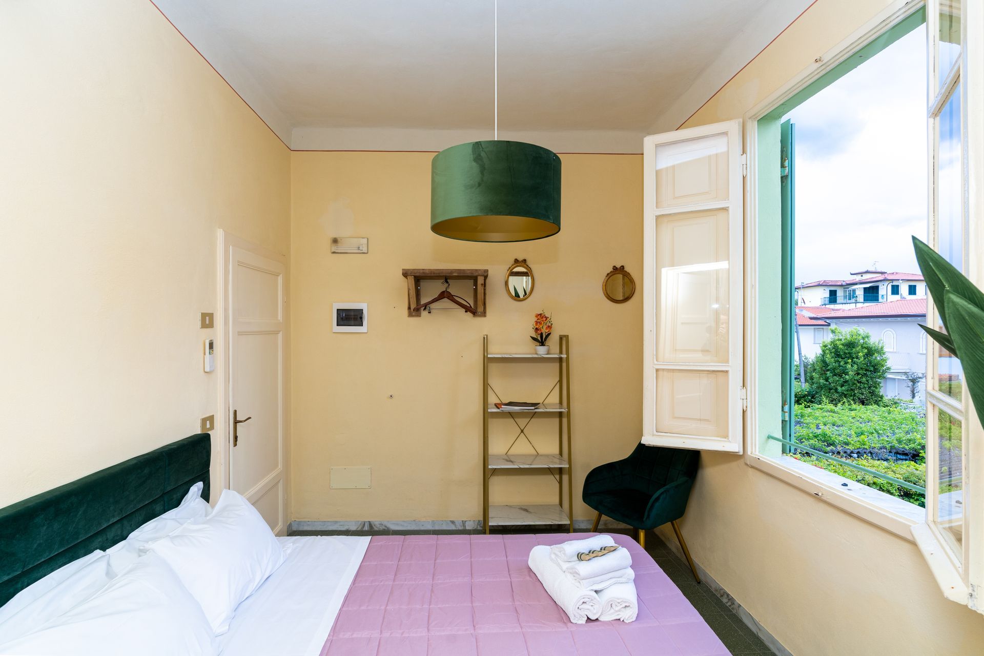 Bedroom with open window, bed, shelves, chair, and a green lampshade.